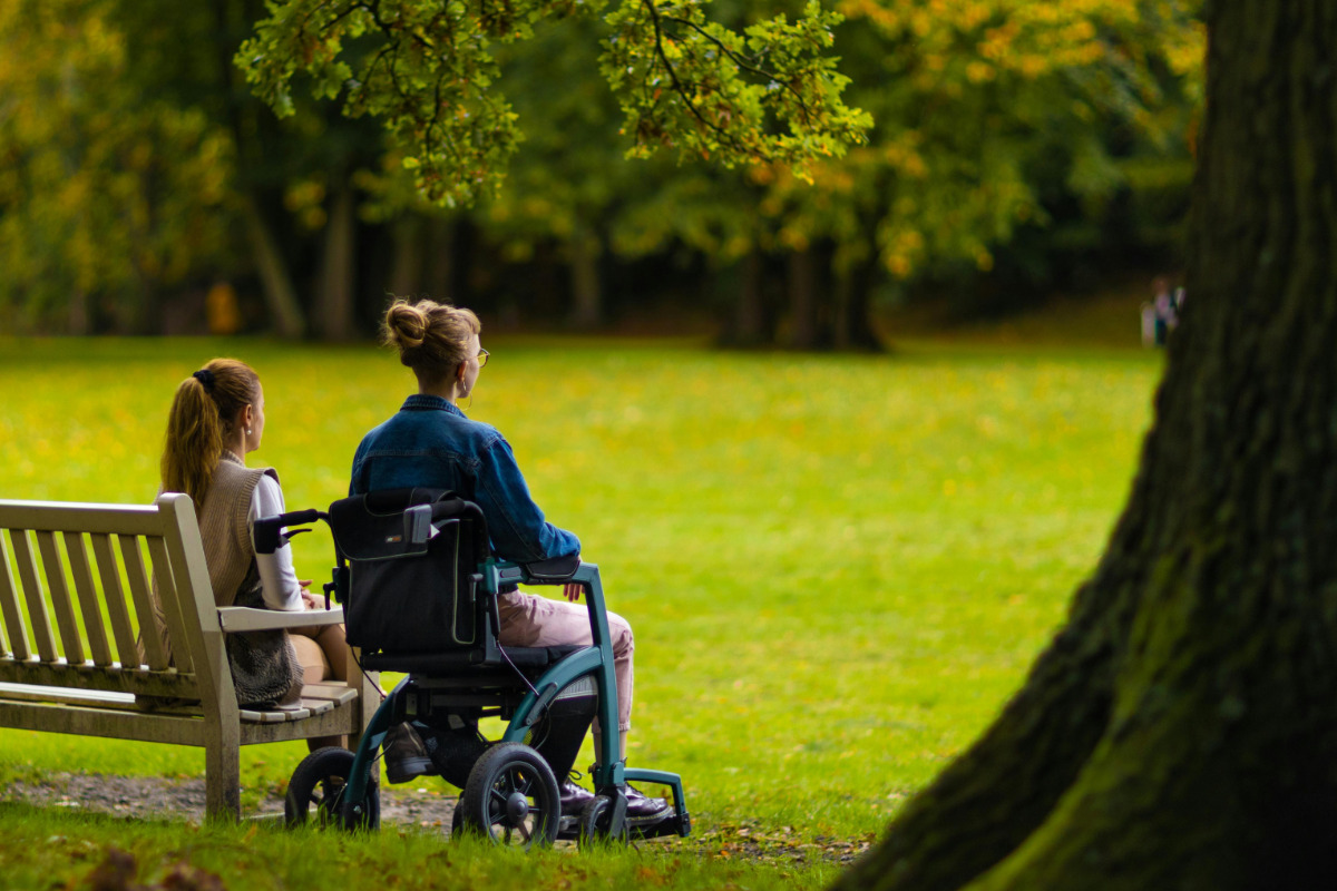 Two women sit in park, one woman in wheelchair